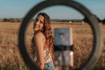 Chica joven guapa posando delante del smartphone sobre un aro de luz en mitad de un campo de trigo...