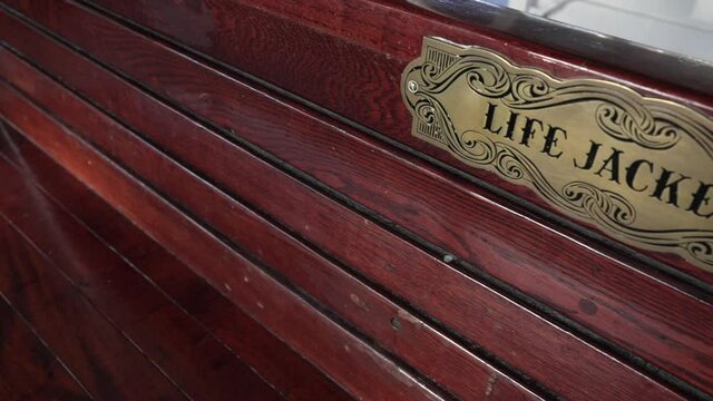 This panning video shows a "Life Jackets" plaque sign on an old steamboat wooden bench.
