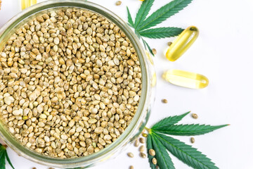 Bowl with Hemp seeds Cannabis leafs and CBD oil capsules isolated on white