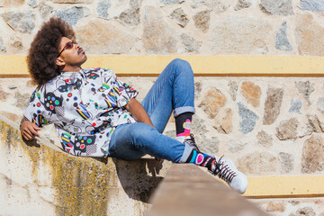 horizontal image of black guy with afro hair and red glasses lying on his side on a wall