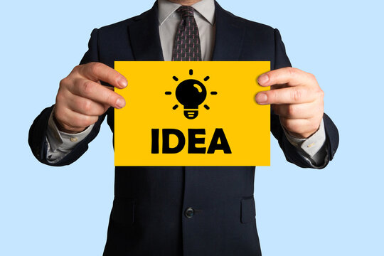 Businessman holding a sheet of paper with picture of light bulb and word idea, all symbolizing idea, innovation, creativity, inspiration, breakthrough, improvement.