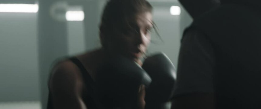 EXTREME CU Portrait of Caucasian female boxer practicing punches with her coach on a boxing ring. Shot with 2x anamorphic lens