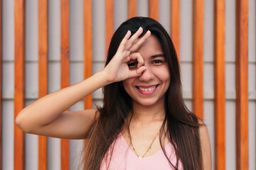 Attractive young woman making the right sign and covering her eye, expresses emotion, model poses outdoors