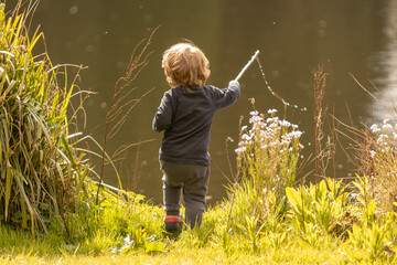 little boy pretend fishing in a lake pictured from his back