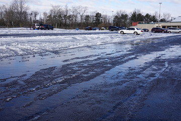 A partially plowed parking lot covered with ice, snow and slush on a sunny day