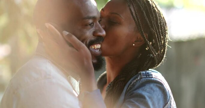 Candid African couple together outside at park. Woman kissing man in cheek outside