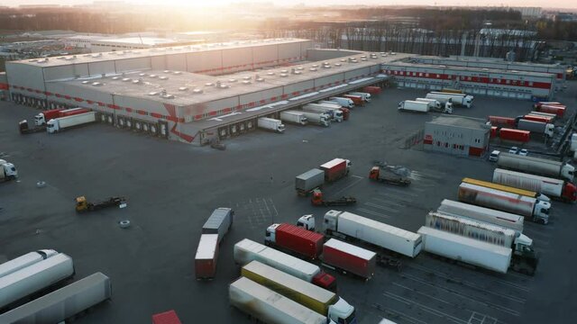 Logistics park with a loading hub. Semi-trailers trucks are parked and waiting for the loading and unloading of goods at the warehouse ramps. Aerial view