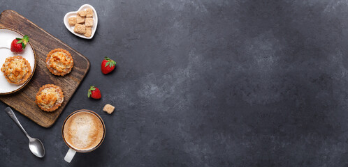 Cup of coffee, cakes and strawberries on a wooden cutting board on dark stone background. Horizontal banner. Top view