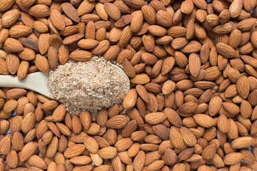 almond flour in wooden spoon over many raw almonds