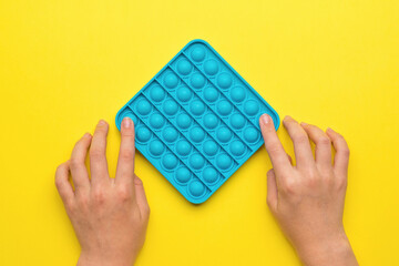 Children's hands with silicone pop it toy on yellow background.