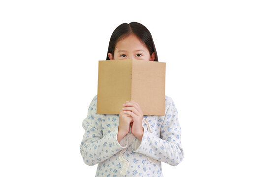 Asian little girl child holding brown book cover hide her mouth and nose with looking at camera isolated over white background. Image with clipping path