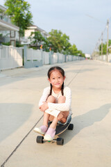 Cute Asian little girl child relax sitting on a skateboard on the street