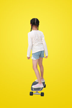 Rear view Asian little girl child riding on skateboard isolated on yellow background. Image with clipping path