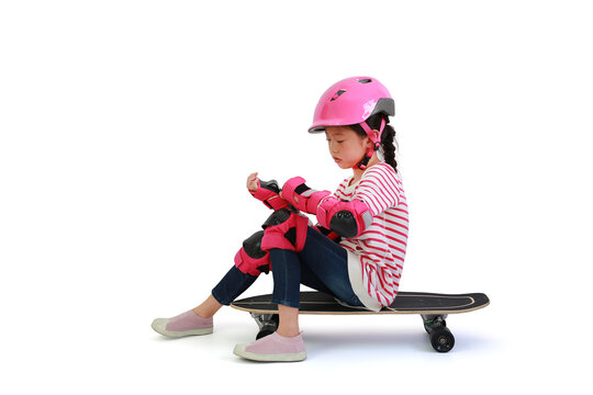 Asian little girl child skateboarder sitting on skateboard with wearing safety and protective equipment isolated on white background. Image with Clipping path