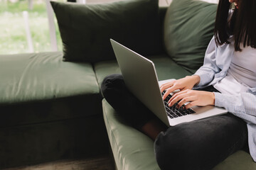 A brunette girl sits on a green sofa and prints something on a laptop