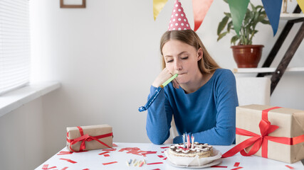 Party is not successful sad caucasian woman is bored sitting alone at the table with cake and...
