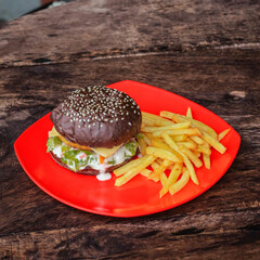 Black burger with French fries in red plate on a rustic wooden serving board