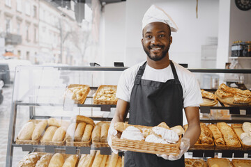 African American baker holding tray of bread in bakery