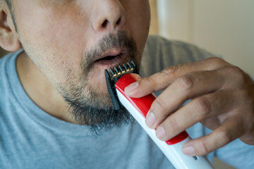 Asian man shaving beard with electric razor machine.
