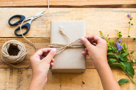 hand of girl making box package prepare send to customer by post office with rope ,scissors  arrangement flat lay style on background wooden