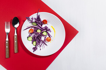 Organic vegetarian salad of vegetable with red cabbage, oil on white plate in sunny day with shadow on red, white wood trend color background.