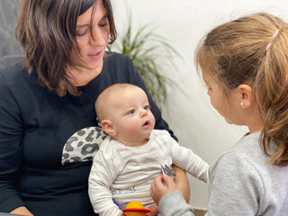 Baby looking attentively at her sister. Mom holding baby.Caucasian family at home.