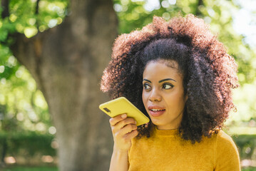 Pretty afro woman sending an audio message on her mobile.