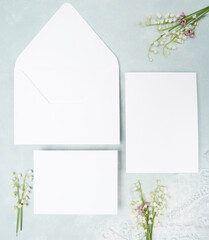 Fresh lily of the valley and blank wedding stationery flat lay on light blue background