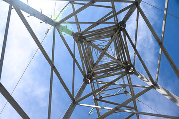 Bottom up view inside a high voltage power tower, against a blue sky with white clouds.