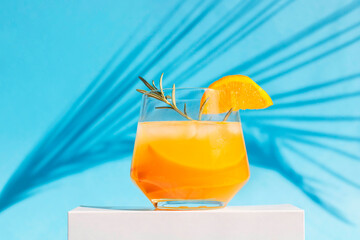 orange cocktail, juice, a drink in a glass glass stands on the podium with the shadow of a palm...