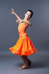Naklejka premium Child girl in an orange sports dress posing in dance movement on gray background