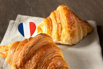 Two fresh french croissants and a heart in the colors of the French flag on a table