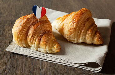 Two fresh french croissants and a heart in the colors of the French flag on a table