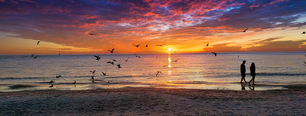 Ein wunderschöner Sonnenuntergang und eine Silhouette eines Paares, das entlang der Küste auf dem Sand spazieren geht, aufgenommen am Clearwater Beach, Florida