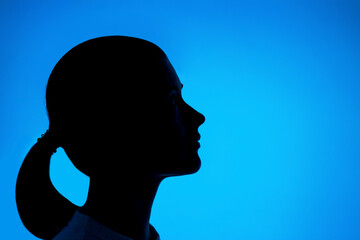 Profile of a dark female silhouette on blue background close-up.