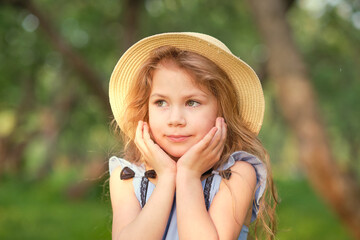 portrait of a young smiling girl, beautiful child outside in a straw hat enjoying a warm day