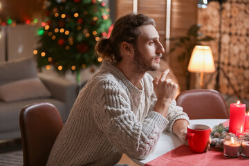 Handsome man sitting at table in room decorated for Christmas