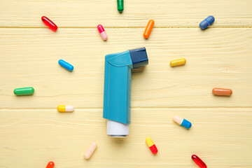 Modern inhaler and pills on color wooden background