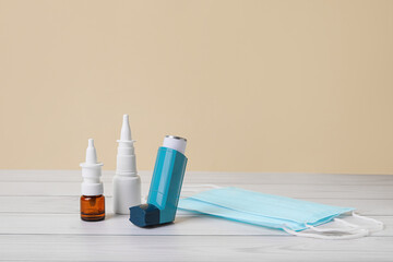 Inhaler with nasal drops and mask on color wooden background