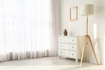 Chest of drawers and lamp near light wall in modern room