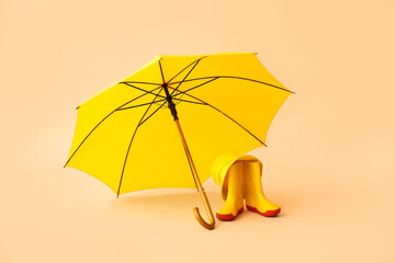 Stylish umbrella and rubber boots on color background