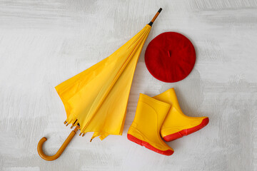 Stylish umbrella, rubber boots and hat on light background