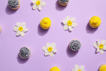 Tasty cupcakes with beautiful narcissus flowers on color background