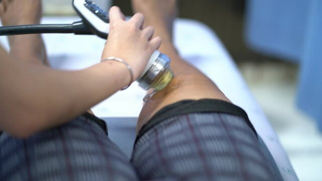 Therapist Doctor is doing shock wave therapy on Knee woman in hospital, Patient is getting Profilaxing Procedure of Physiotherapist. Health, Medicine.