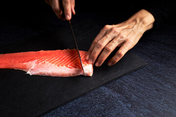 Female cook preparing a piece of Salmon to make sushi. Asian food concept