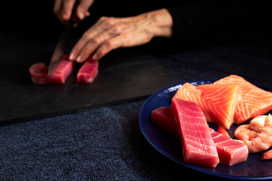 Female cook preparing some pieces of bluefin tuna and salmon to make sushi.
