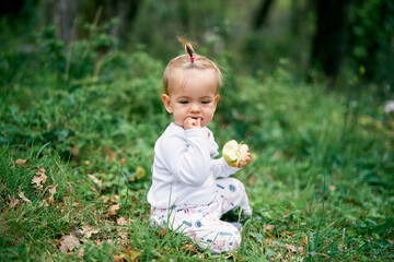 Little baby girl sitting on a green meadow with an apple in her hand