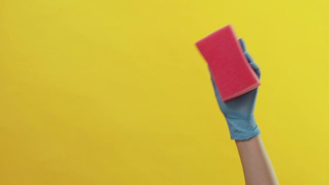 Tidy cleaning. Washing tools. Surface hygiene. Invisible dirtiness. Unrecognizable woman protective gloves using pink soapy sponge isolated yellow background copy space.