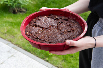 young woman holding a round silicone tray of chocolate brownie before picnic in garden
