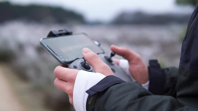 Close up hand of a man that controls remote drone controller with a mobile phone